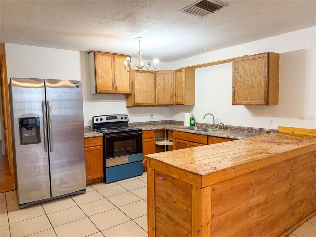 A kitchen features wood cabinets, a stainless steel refrigerator, a black stove, and a counter — 308 CENTRAL AVENUE, FROSTPROOF, FL