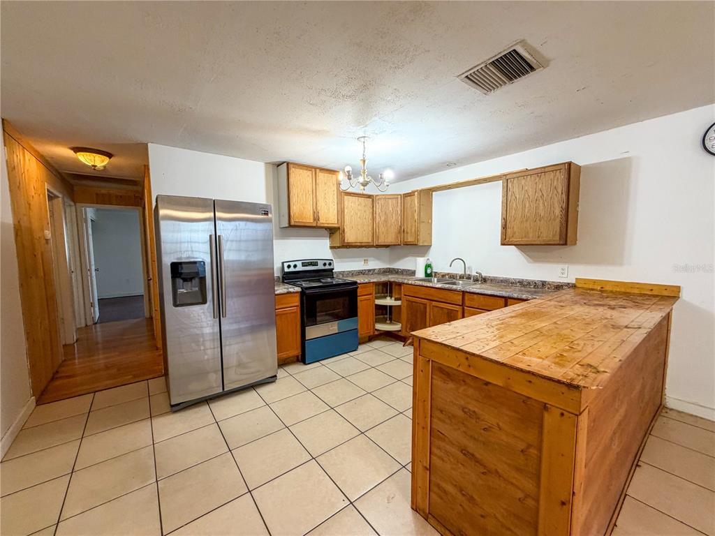 A kitchen features wood cabinets, a stainless steel refrigerator, tile flooring, and a wooden island — 308 CENTRAL AVENUE, FROSTPROOF, FL