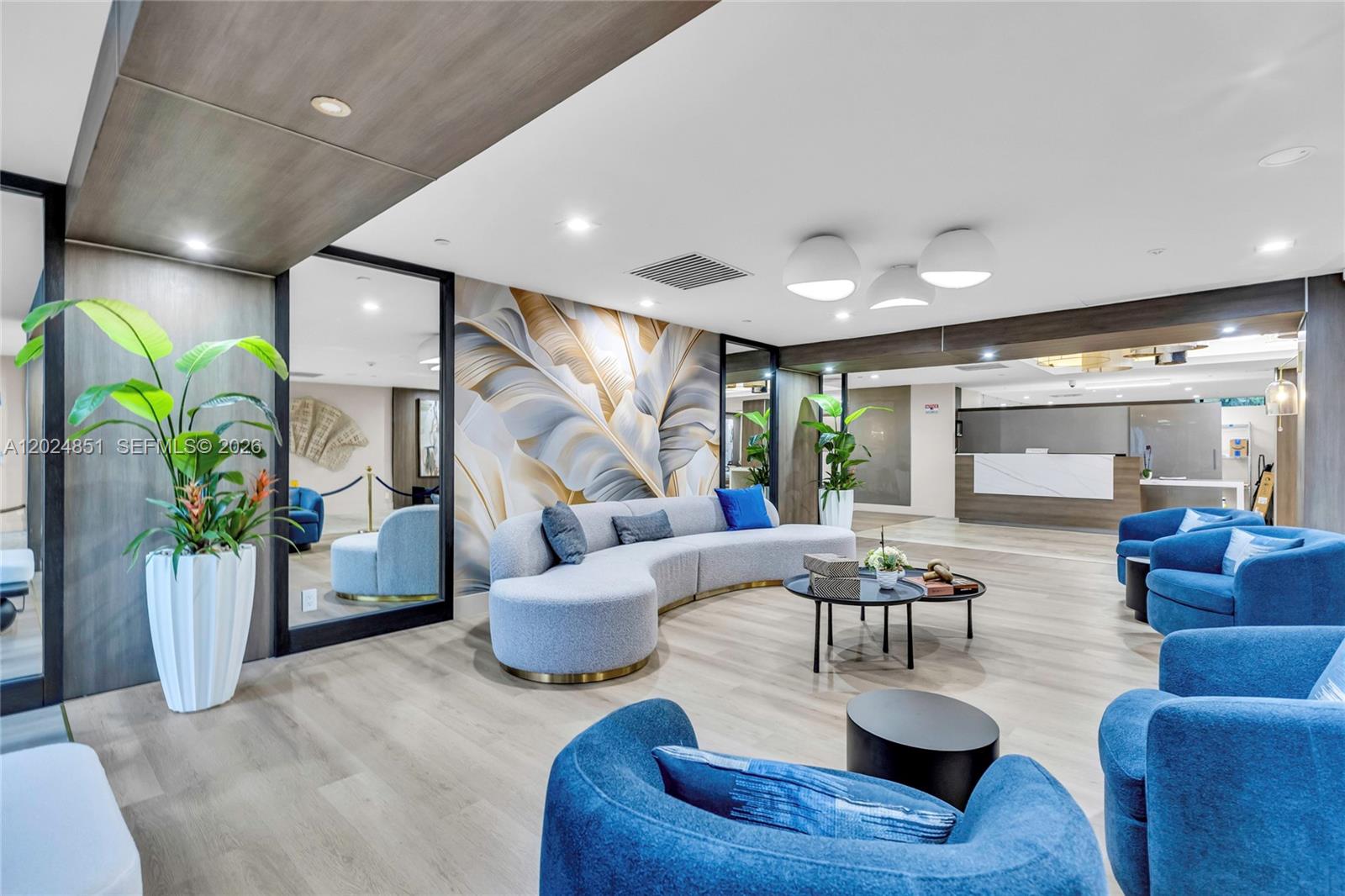 A modern lobby features a curved gray sofa, blue armchairs, and a large leaf-patterned mural — 4200 Hillcrest Dr # 504, Hollywood FL 33021, HOLLYWOOD, FL
