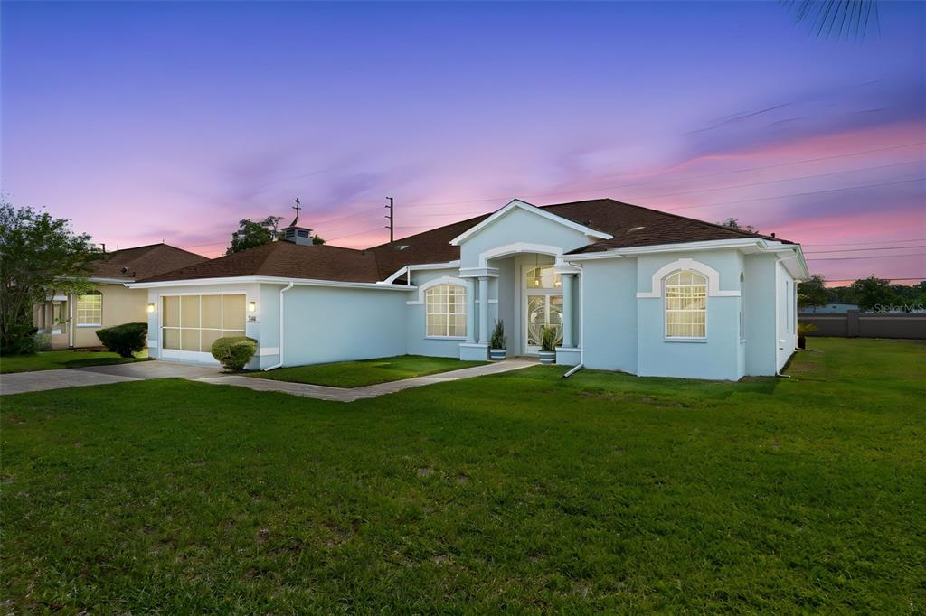 A light blue single-story house with a brown roof and a front-facing garage at sunset — 3362 ST IVES BOULEVARD, SPRING HILL, FL