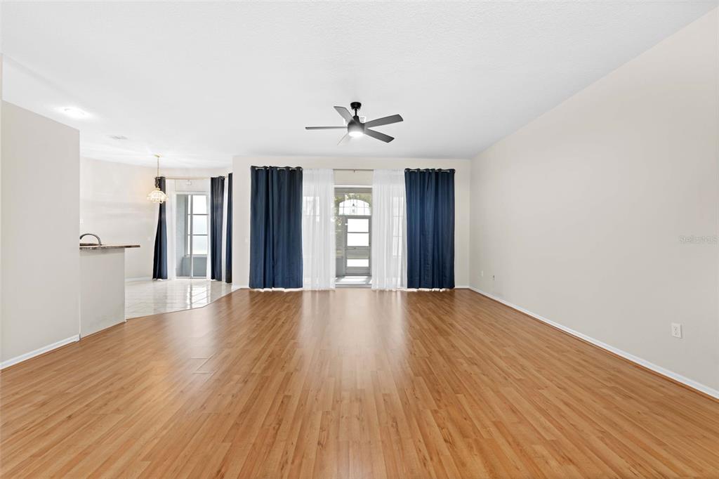 A spacious living room features wood-look flooring, a ceiling fan, and a glass sliding door — 3362 ST IVES BOULEVARD, SPRING HILL, FL