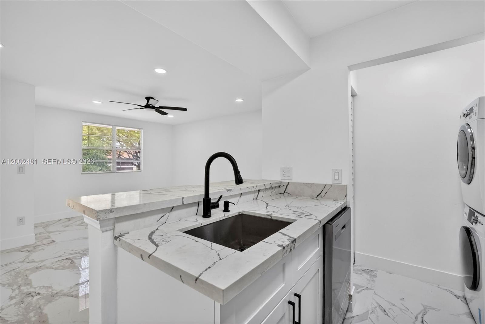 A kitchen features white marble countertops, a black faucet, and a stacked washer and dryer — 1227 SW 46th Ave # 314, Pompano Beach FL 33069, POMPANO BEACH, FL