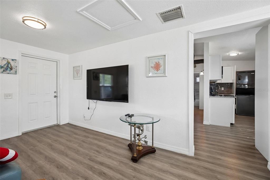 A living room with wood-look flooring, a wall-mounted television, and an open doorway to a kitchen — 2321 EDNOR STREET, PORT CHARLOTTE, FL