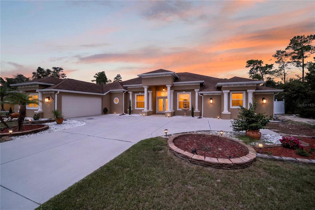 A single-story tan house with a two-car garage and a concrete driveway at sunset — 10202 SW 41ST TERRACE, OCALA, FL