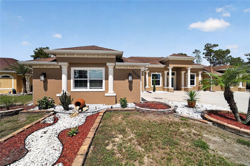 A tan single-story house with a white-trimmed window, columns, and a decorative rock garden — 10202 SW 41ST TERRACE, OCALA, FL
