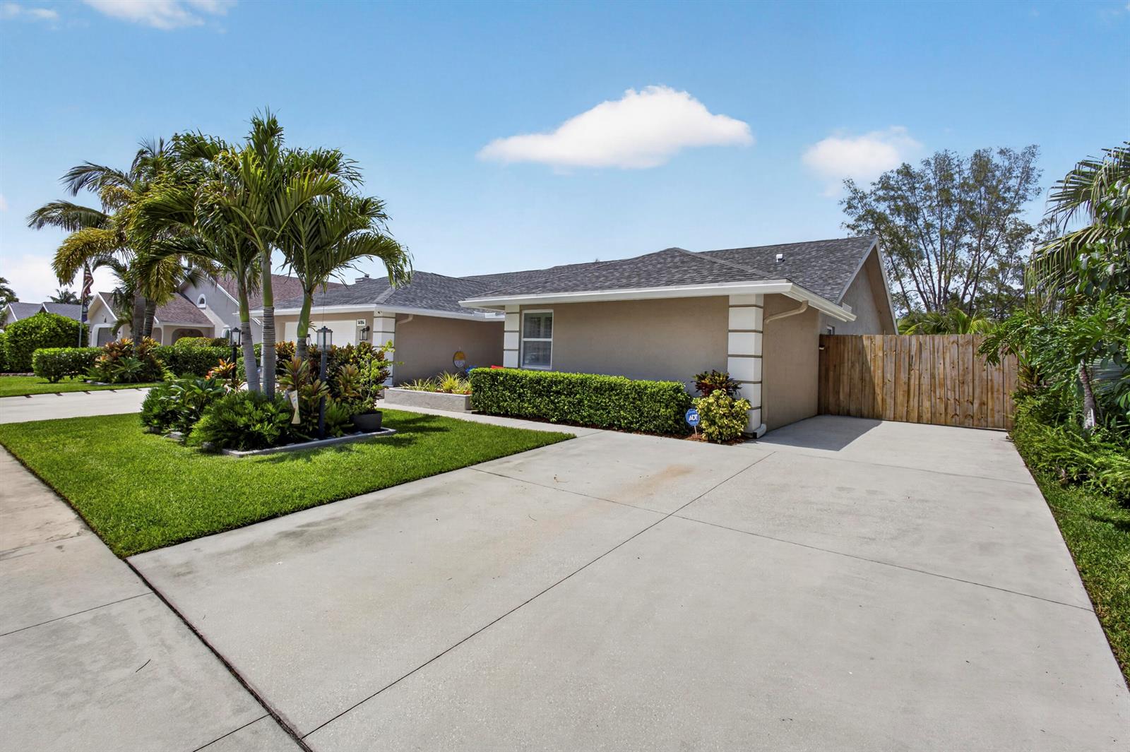 A single-story house with a concrete driveway, palm trees, and a wooden privacy fence — 14184 Aster Avenue, Wellington FL 33414, WELLINGTON, FL