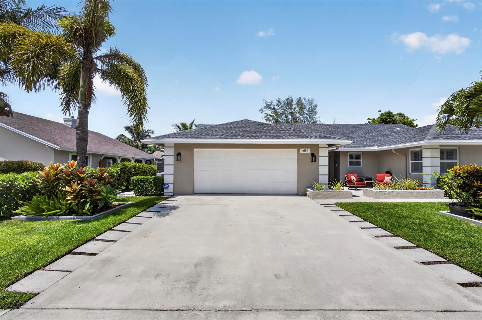 A single-story house features a white garage door, a concrete driveway, and palm trees — 14184 Aster Avenue, Wellington FL 33414, WELLINGTON, FL