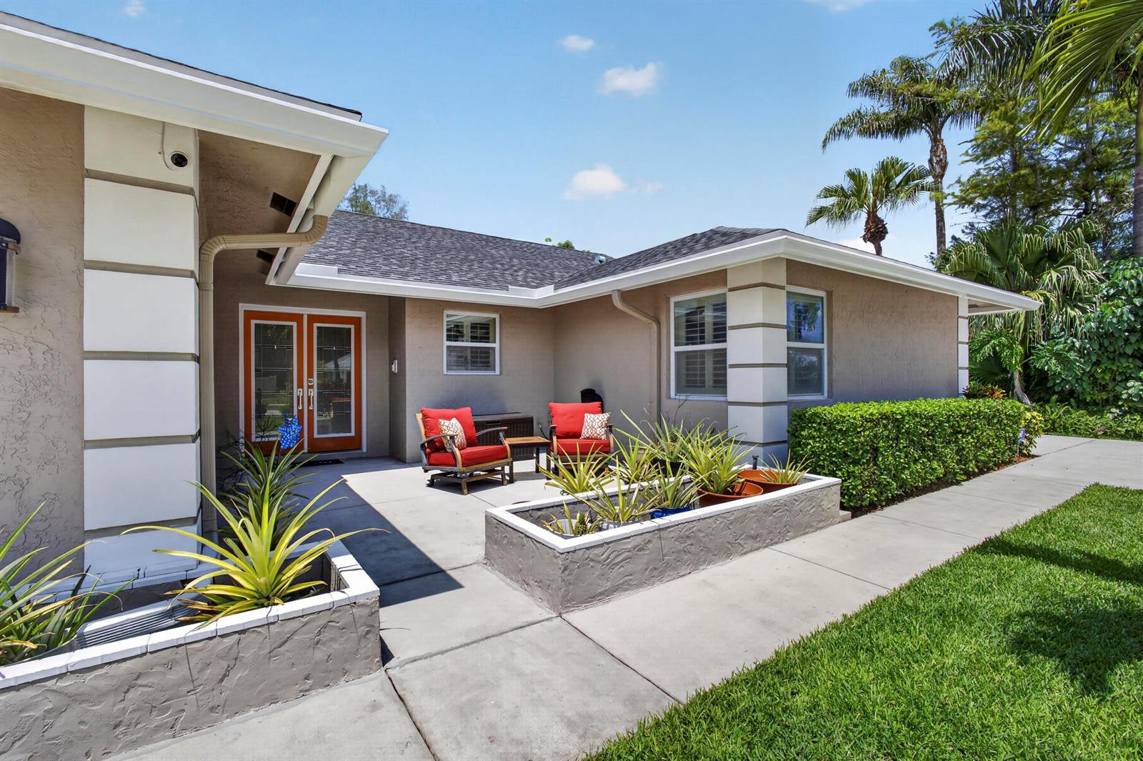 A patio with two red chairs and a concrete planter sits outside a tan house — 14184 Aster Avenue, Wellington FL 33414, WELLINGTON, FL