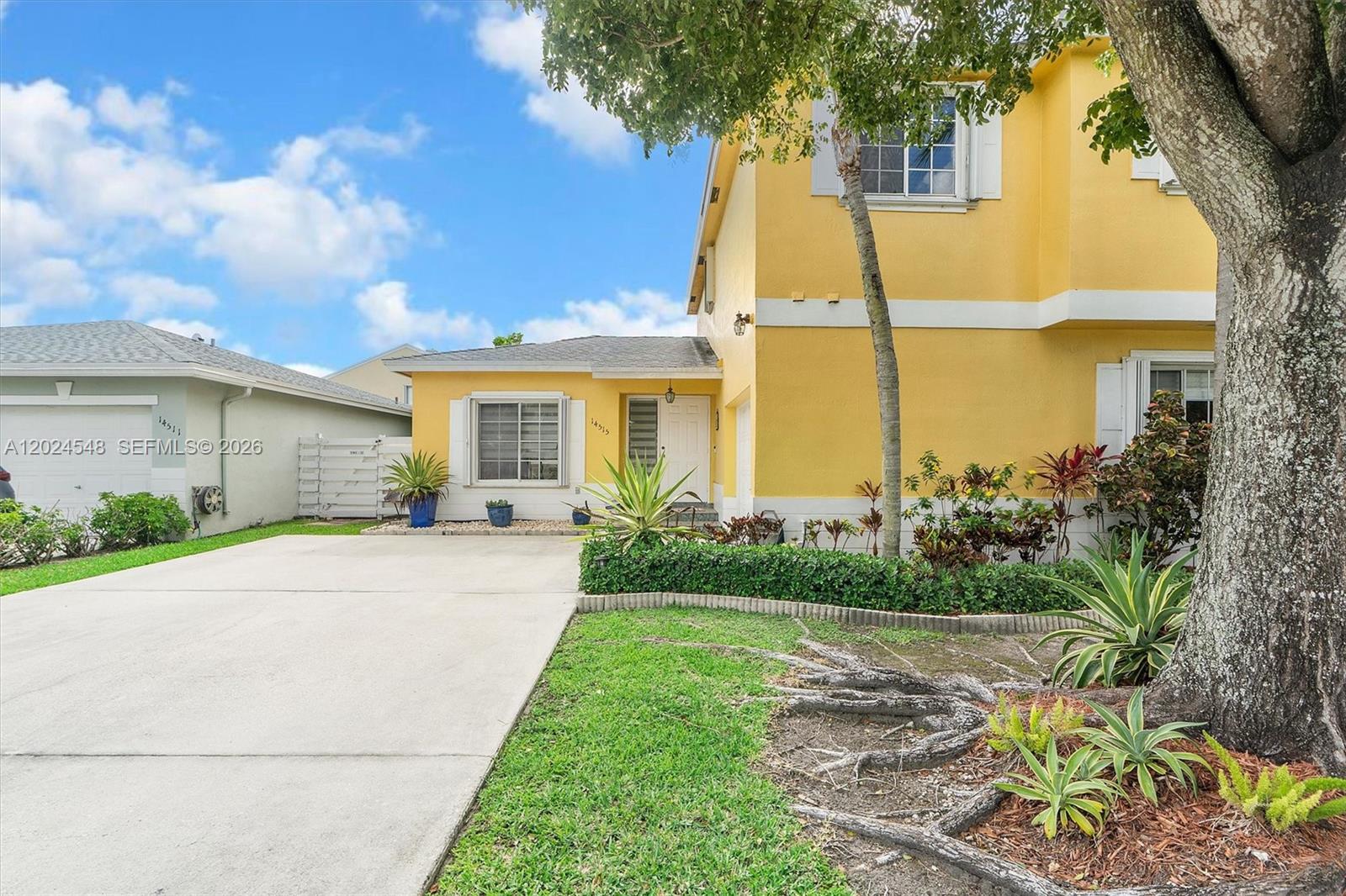 A yellow two-story house features a concrete driveway, a front lawn, and mature landscaping — 14515 SW 139th Ave Cir E, Miami FL 33186, MIAMI, FL