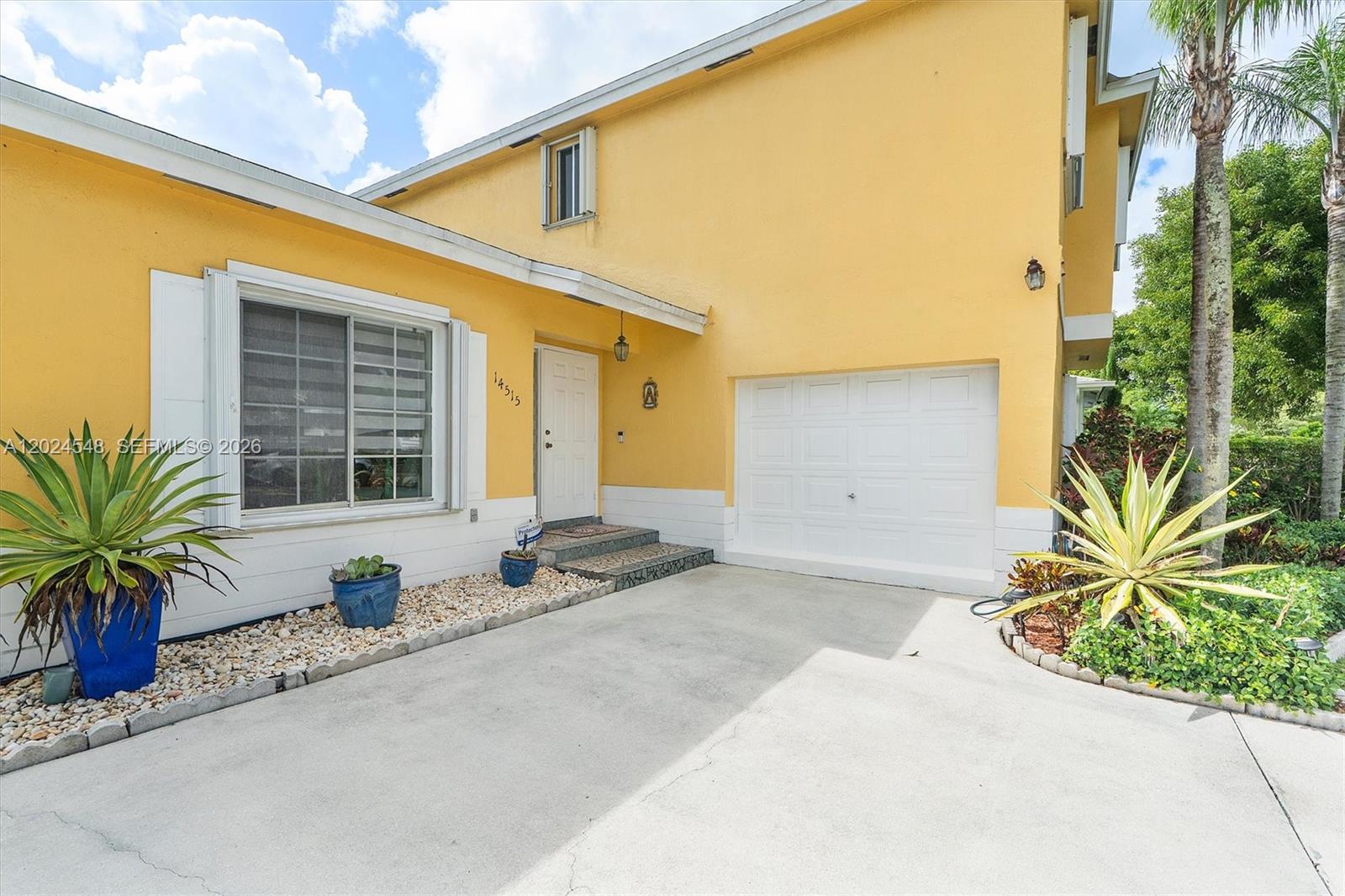A yellow two-story house features a white garage door, a front entrance, and landscaping — 14515 SW 139th Ave Cir E, Miami FL 33186, MIAMI, FL