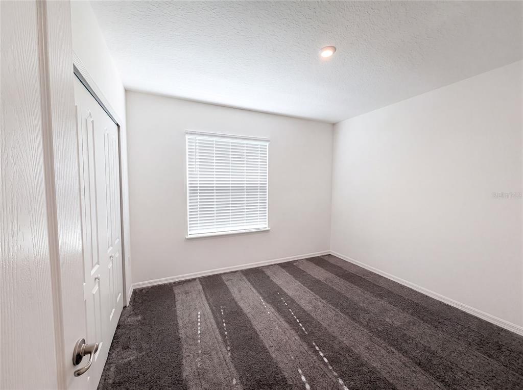 An empty bedroom features white walls, a window with blinds, and gray striped carpeting — 1443 GENERAL CUSTER AVENUE, DAYTONA BEACH, FL