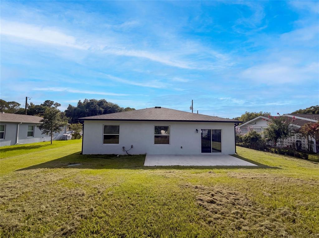 The rear exterior of a single-story house features a concrete patio and a grassy yard — 1443 GENERAL CUSTER AVENUE, DAYTONA BEACH, FL