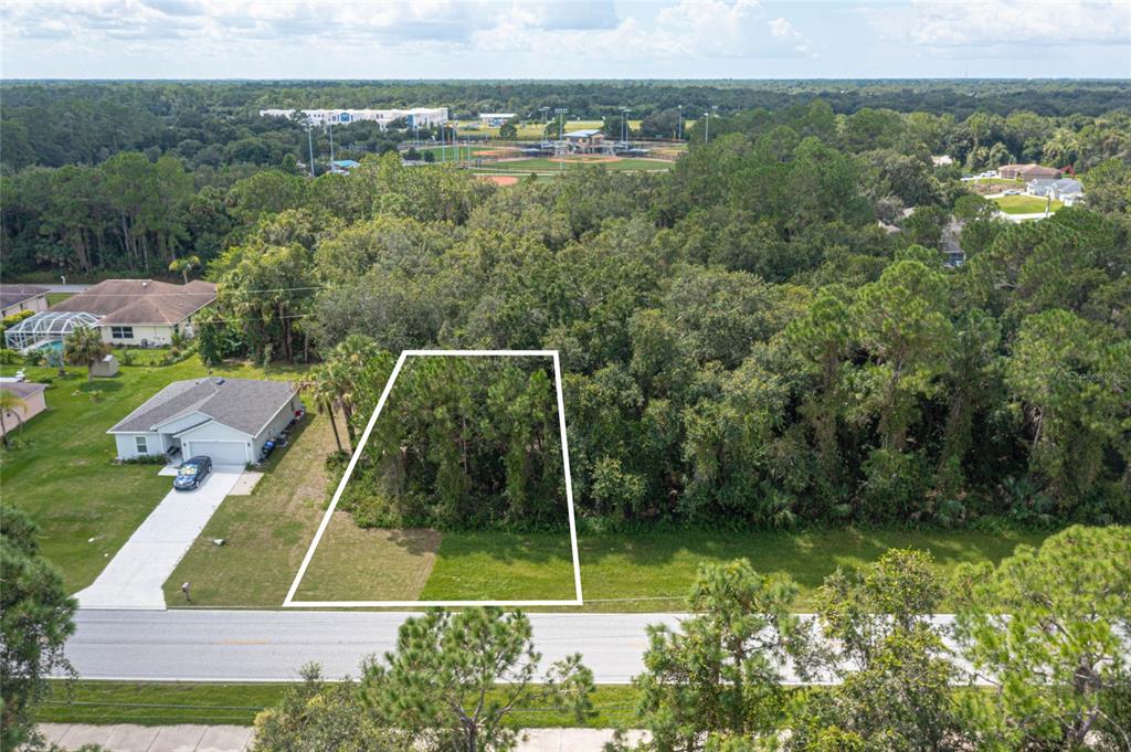 An aerial view shows a vacant, wooded residential lot outlined in white next to a house — E PRICE BOULEVARD LOT 7, NORTH PORT, FL