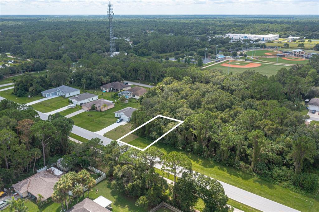 An aerial view shows a vacant, rectangular residential lot outlined in white amidst a wooded area — E PRICE BOULEVARD LOT 7, NORTH PORT, FL