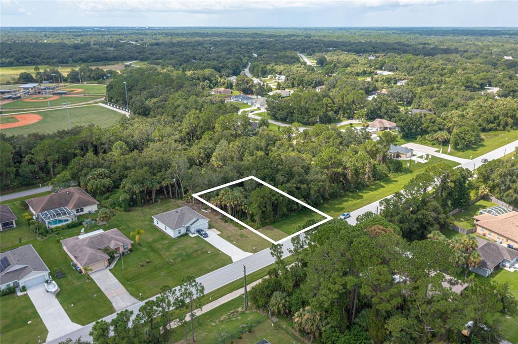 An aerial view shows a vacant, wooded residential lot outlined in white next to existing houses — E PRICE BOULEVARD LOT 7, NORTH PORT, FL