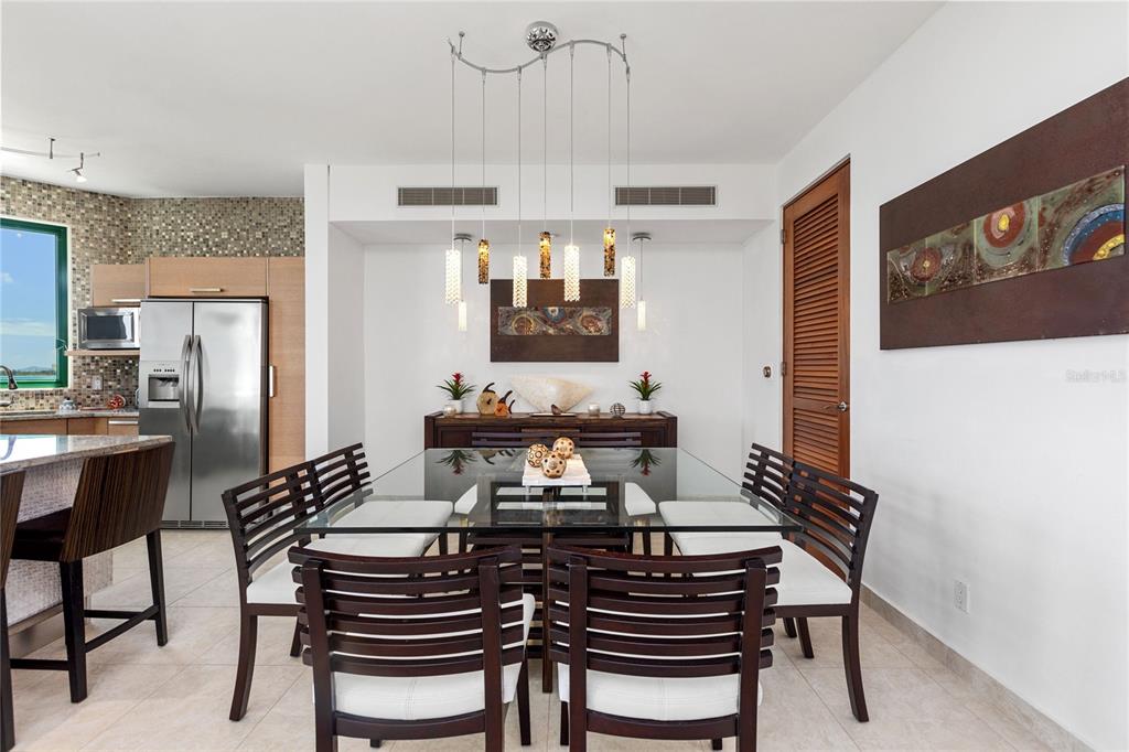 A dining room features a glass-topped table, slatted wooden chairs, and a modern pendant light — 9000 RIO MAR UNIT 263, RIO GRANDE, PR