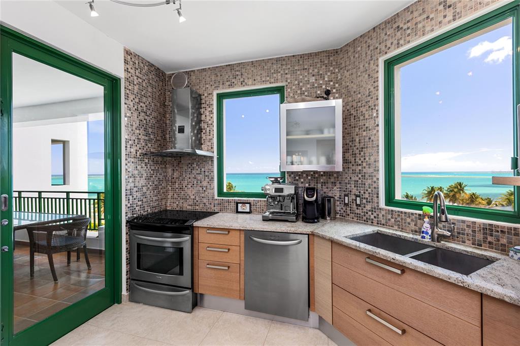 A kitchen with wood cabinets, stainless steel appliances, mosaic tile walls, and ocean views — 9000 RIO MAR UNIT 263, RIO GRANDE, PR
