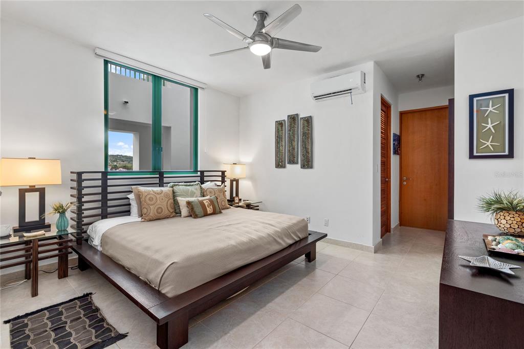 A bedroom features a platform bed, ceiling fan, tile flooring, and a view of hills — 9000 RIO MAR UNIT 263, RIO GRANDE, PR