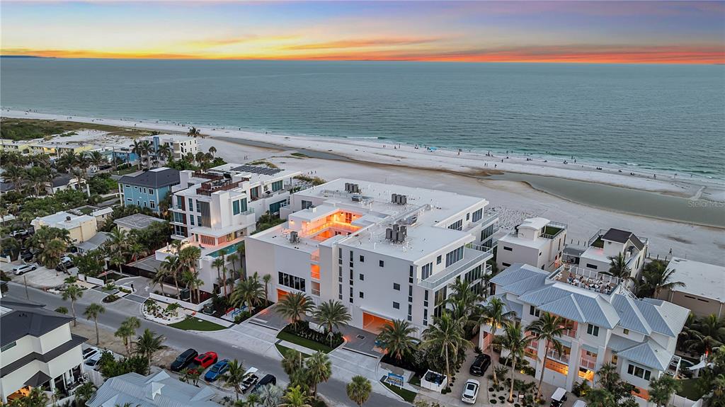 An aerial view shows a modern white multi-story building located directly on a sandy beach — 70 AVENIDA VENECCIA UNIT 204, SARASOTA, FL