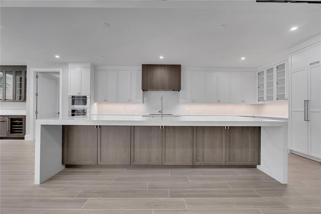 A modern kitchen features a large white-topped island with wood cabinetry and white upper cabinets — 70 AVENIDA VENECCIA UNIT 204, SARASOTA, FL