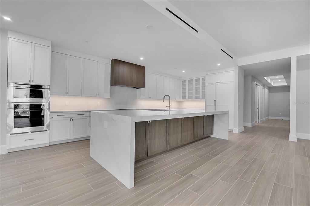 A modern kitchen features white cabinetry, a large marble-topped island, and wood-look tile flooring — 70 AVENIDA VENECCIA UNIT 204, SARASOTA, FL