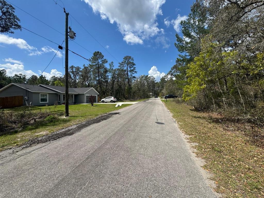 A paved road runs through a residential area with a house and wooded lots — MALAUKA PASS CIRCLE, OCKLAWAHA, FL
