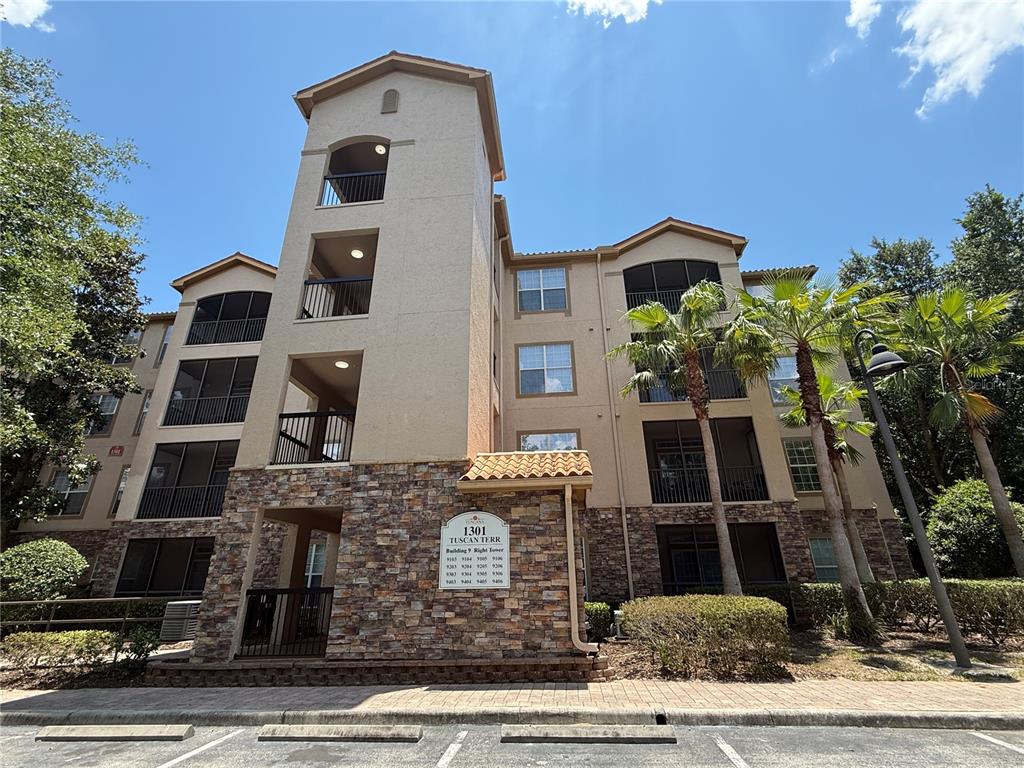 A multi-story apartment building features a stone-clad entrance, screened balconies, and palm trees — 1301 TUSCAN TERRACE UNIT 9306, DAVENPORT, FL