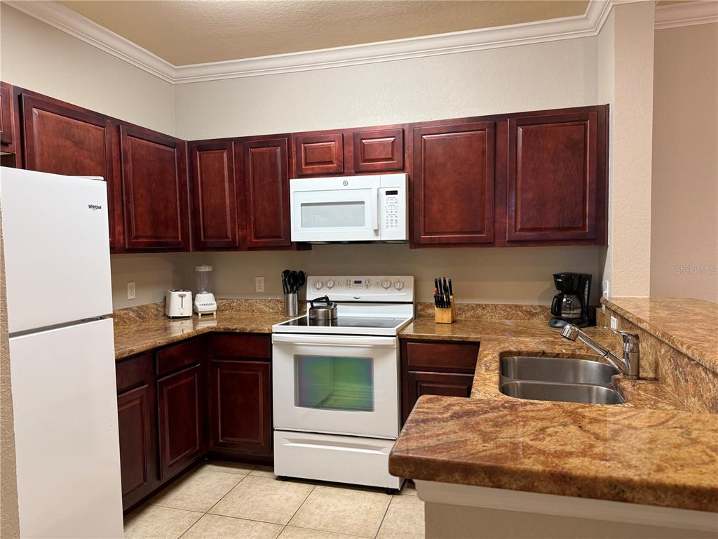A kitchen features dark wood cabinets, granite countertops, and white appliances — 1301 TUSCAN TERRACE UNIT 9306, DAVENPORT, FL