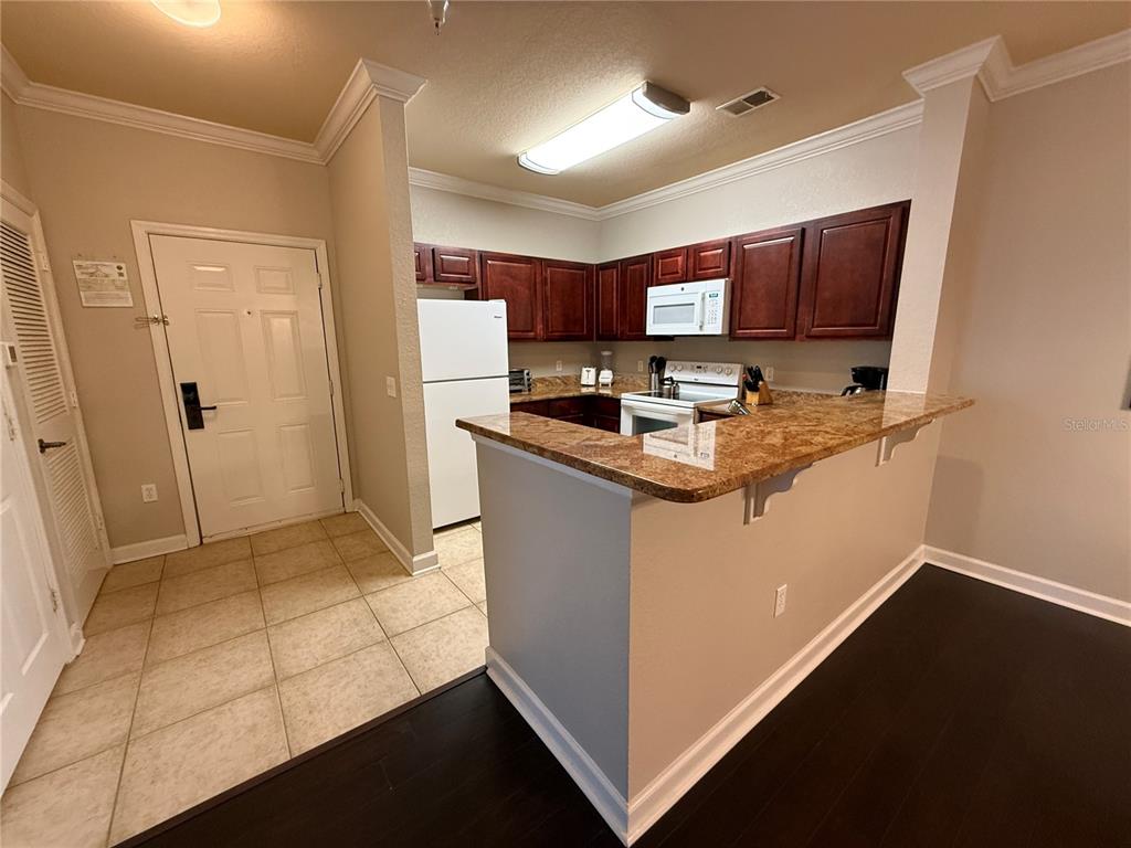 A kitchen features dark wood cabinets, granite countertops, white appliances, and a breakfast bar — 1301 TUSCAN TERRACE UNIT 9306, DAVENPORT, FL