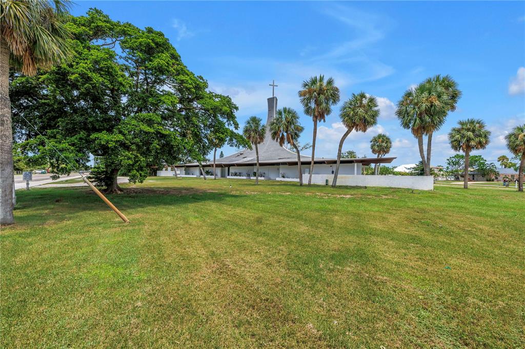 A white church building with a tall steeple stands on a grassy lot with palm trees — 6608 MARINA DRIVE, HOLMES BEACH, FL