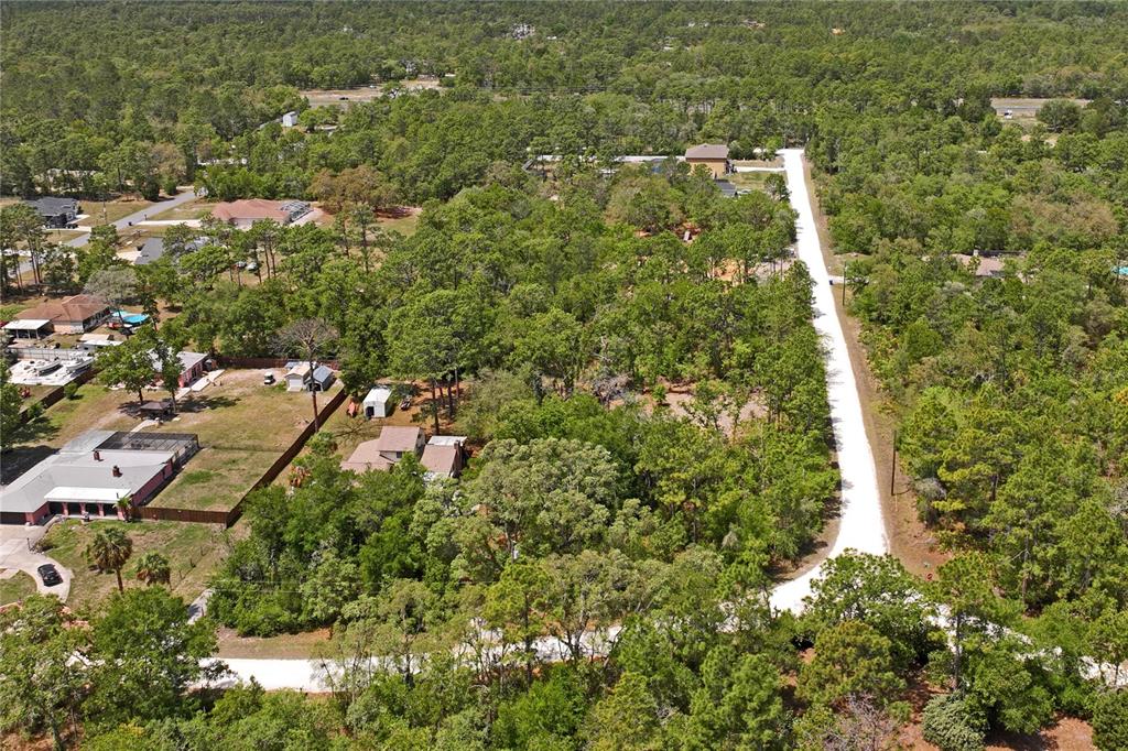 An aerial view shows a long, white gravel driveway winding through a wooded residential area — 0 YELLOWSTONE AVENUE, WEEKI WACHEE, FL