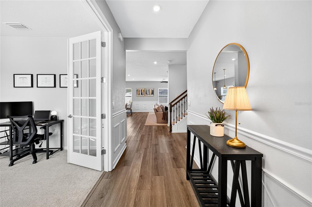 A hallway with wood-look flooring leads past a home office to a living area — 10196 AGAVE COURT, LAND O LAKES, FL