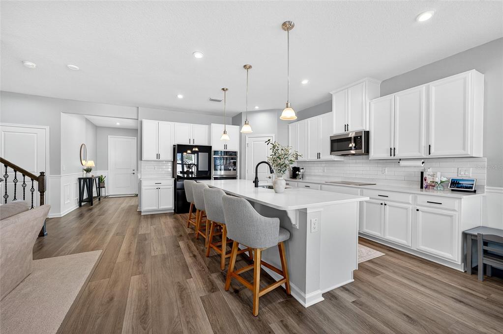 A modern kitchen features white cabinetry, a large center island with bar seating, and wood-look flooring — 10196 AGAVE COURT, LAND O LAKES, FL