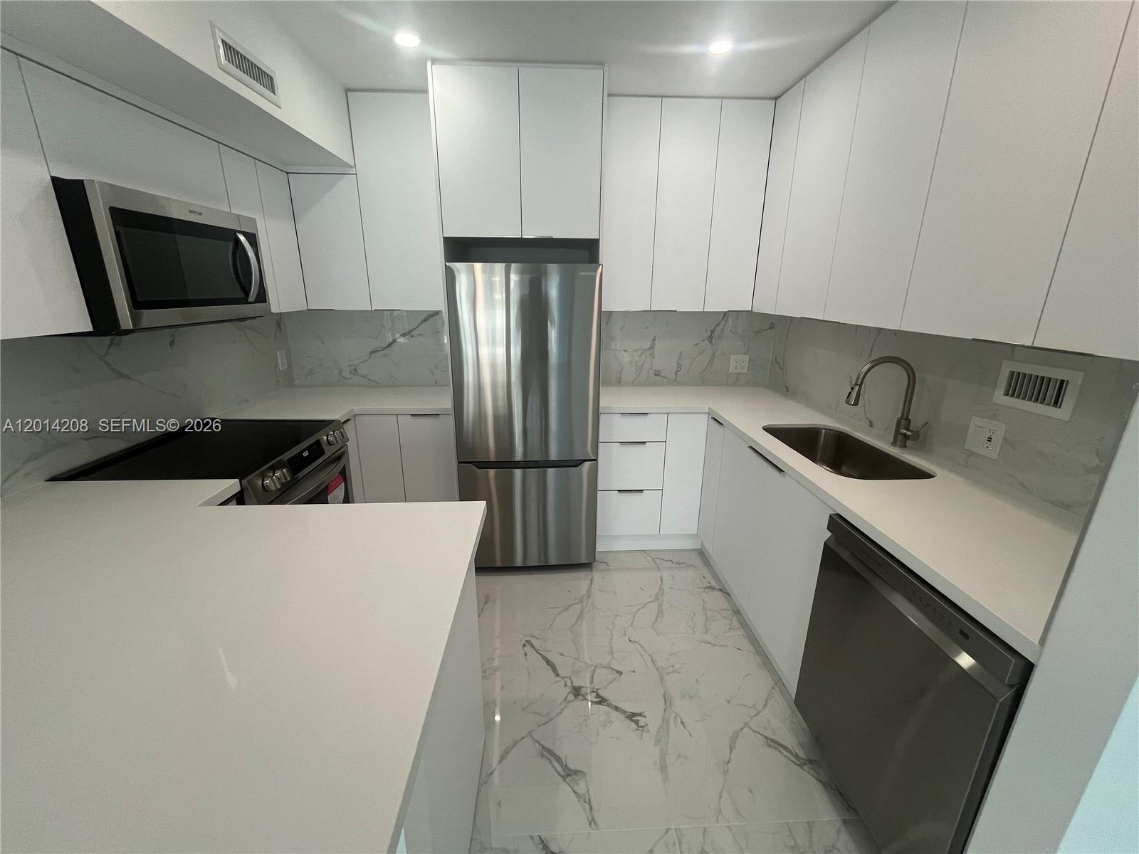 A modern kitchen features white flat-panel cabinets, stainless steel appliances, and marble-patterned tile flooring — 3505 S Ocean Dr # 210, Hollywood FL 33019, HOLLYWOOD, FL