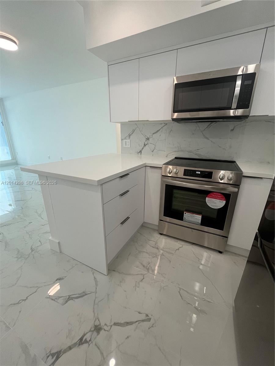 A modern kitchen features white cabinets, stainless steel appliances, and marble-patterned flooring — 3505 S Ocean Dr # 210, Hollywood FL 33019, HOLLYWOOD, FL