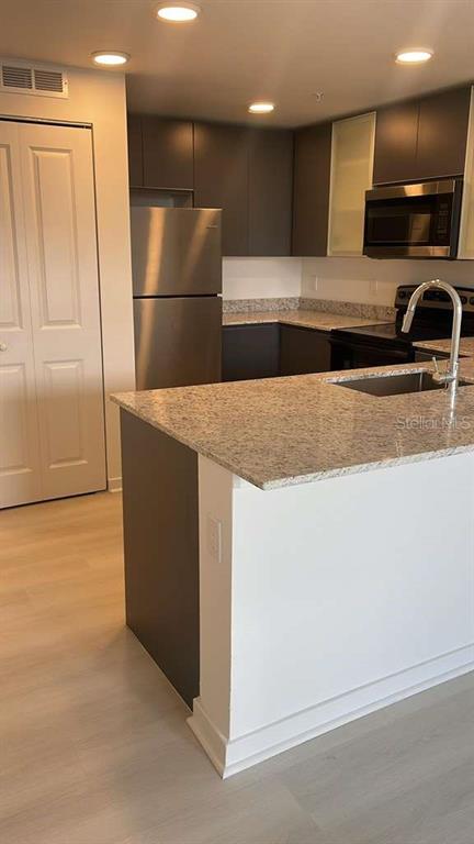 A modern kitchen features a granite-topped island, stainless steel appliances, and dark cabinetry — 5587 MILLENIA PARK BOULEVARD UNIT 111, ORLANDO, FL