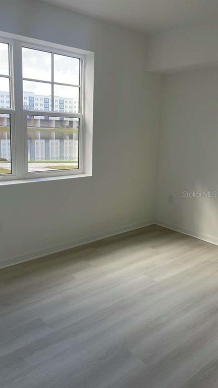 An empty room with light-colored wood-look flooring and a window overlooking a nearby building — 5587 MILLENIA PARK BOULEVARD UNIT 111, ORLANDO, FL