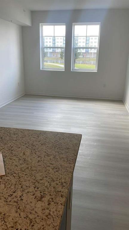 An interior view of a room with light wood-look flooring and two windows overlooking buildings — 5587 MILLENIA PARK BOULEVARD UNIT 111, ORLANDO, FL