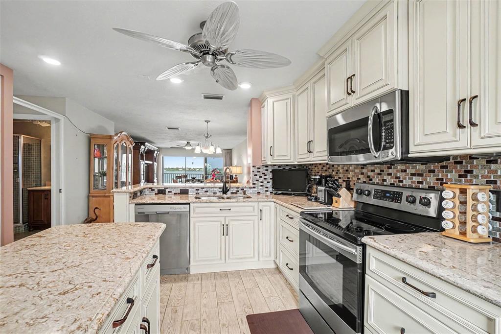 A kitchen with white cabinets, granite countertops, stainless steel appliances, and a ceiling fan — 9011 MIDNIGHT PASS ROAD UNIT 329, SARASOTA, FL