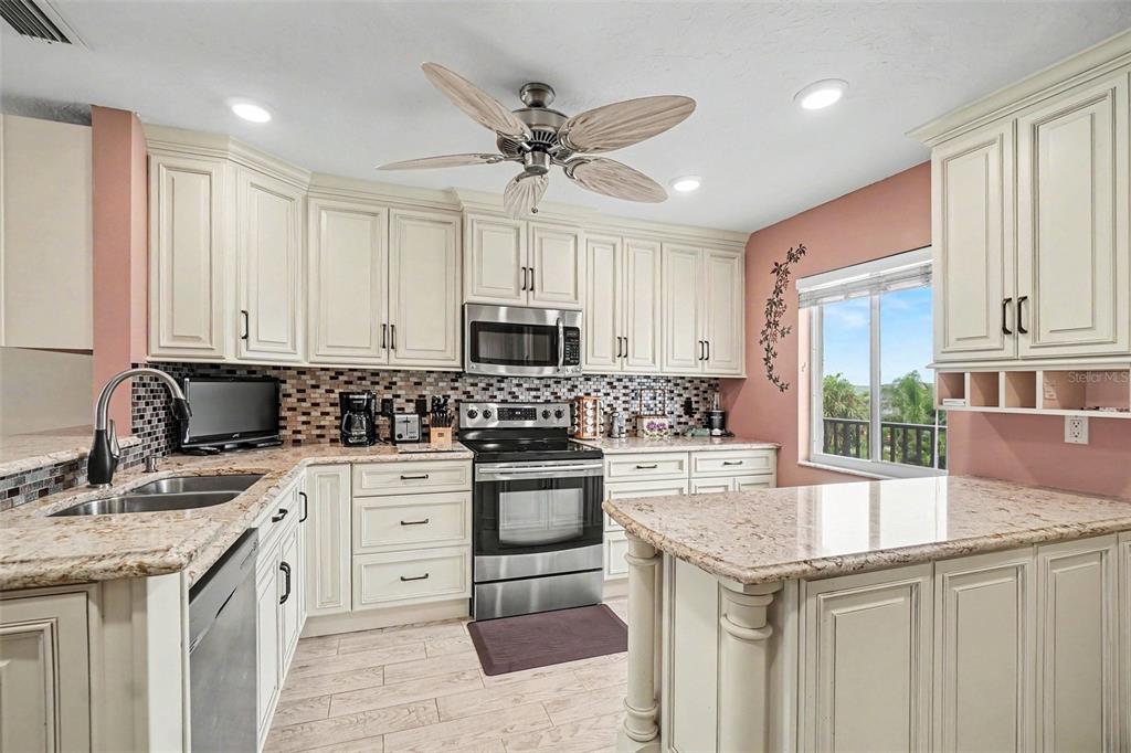 A kitchen features cream-colored cabinets, granite countertops, stainless steel appliances, and a ceiling fan — 9011 MIDNIGHT PASS ROAD UNIT 329, SARASOTA, FL
