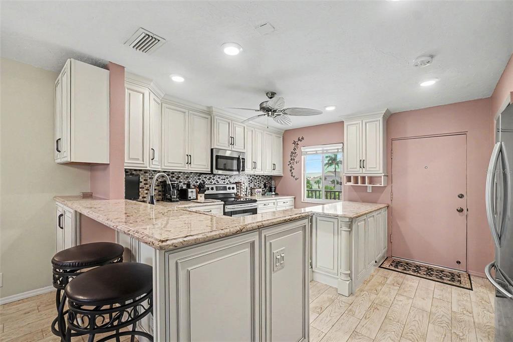 A kitchen features white cabinets, granite countertops, a breakfast bar, and pink walls — 9011 MIDNIGHT PASS ROAD UNIT 329, SARASOTA, FL