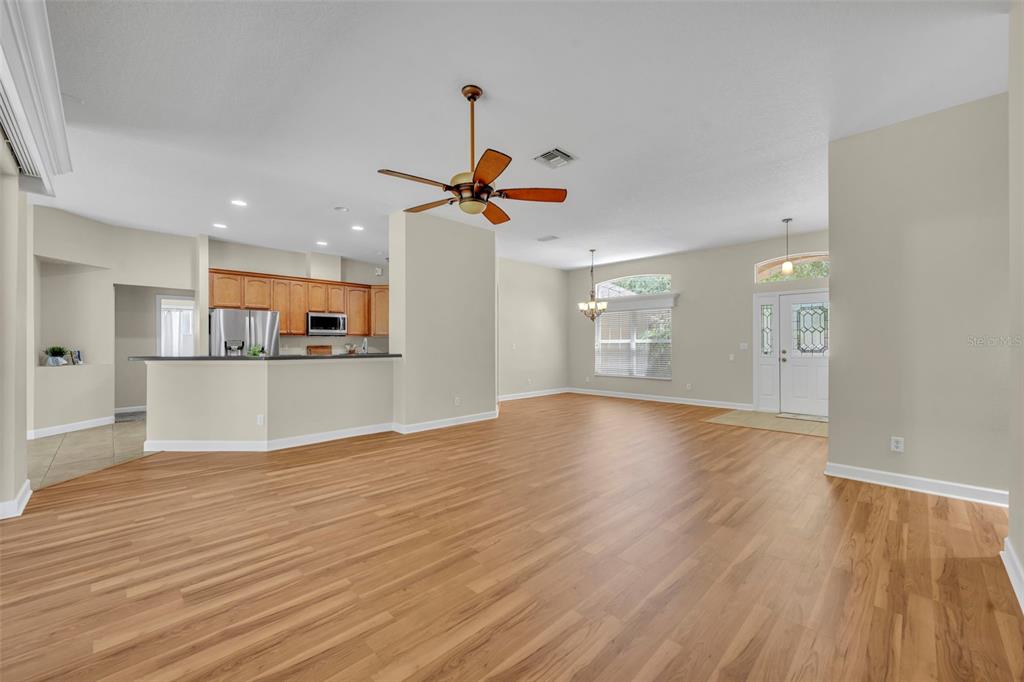An open-concept living area features light wood-look flooring, a ceiling fan, and a kitchen island — 8923 BRIDGEPORT BAY CIRCLE, MOUNT DORA, FL