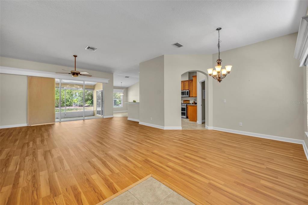 An open-concept living and dining area features light wood flooring, a ceiling fan, and chandelier — 8923 BRIDGEPORT BAY CIRCLE, MOUNT DORA, FL