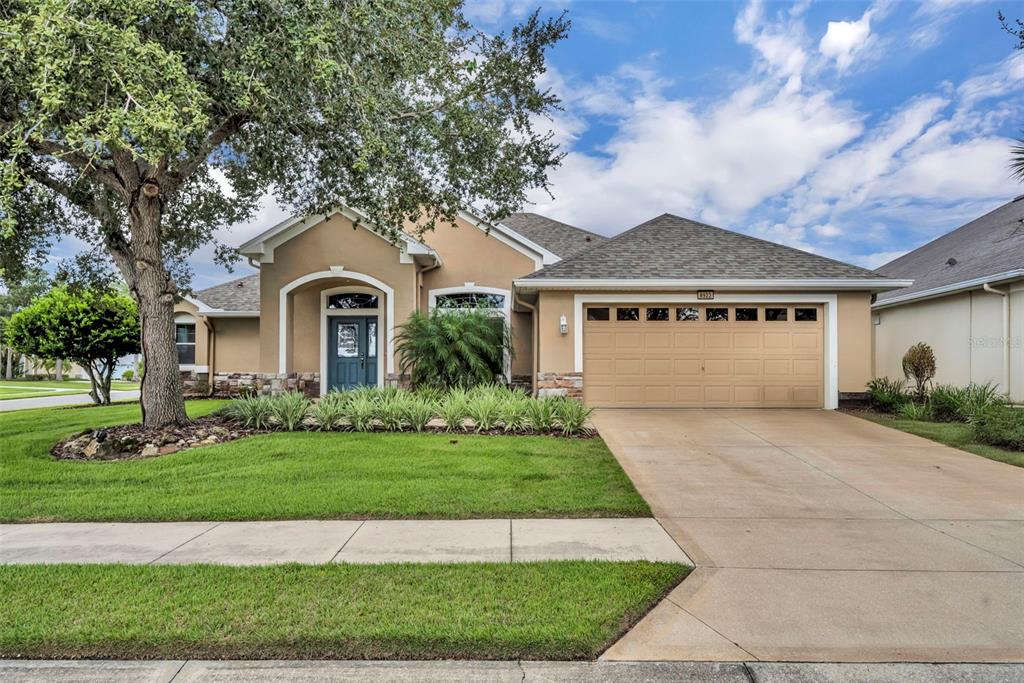 A single-story tan house with a two-car garage, stone accents, and a large front tree — 8923 BRIDGEPORT BAY CIRCLE, MOUNT DORA, FL