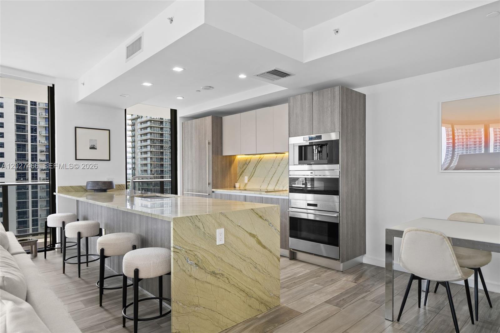 A modern kitchen features a stone island, stainless steel appliances, and views of city skyscrapers — 801 S Miami Ave # 2901, Miami FL 33130, MIAMI, FL