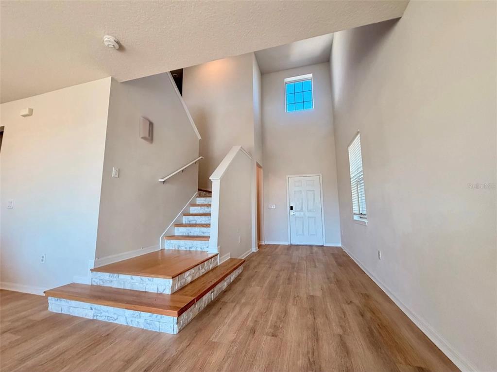An entryway features wood-look flooring, a staircase with stone risers, and a high ceiling — 11415 GREEN HARVEST DRIVE, RIVERVIEW, FL