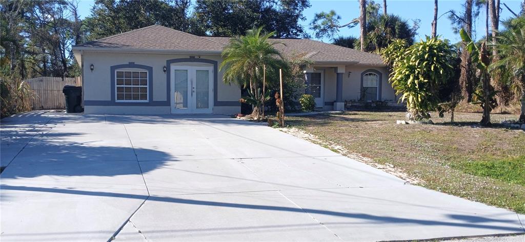 A single-story house with a large concrete driveway, double front doors, and surrounding palm trees — 5573 GAGNON TERRACE, NORTH PORT, FL