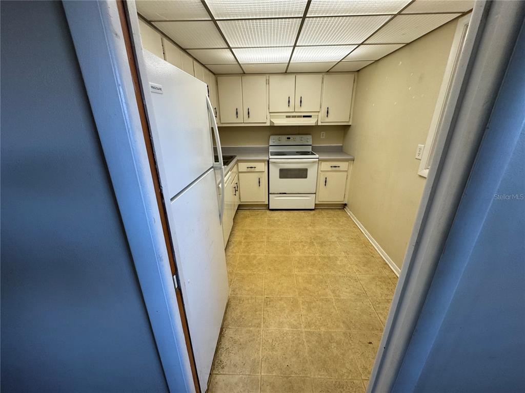 A galley kitchen features white cabinets, white appliances, and a drop ceiling with fluorescent lighting — 245 CENTER ROAD UNIT 211, VENICE, FL