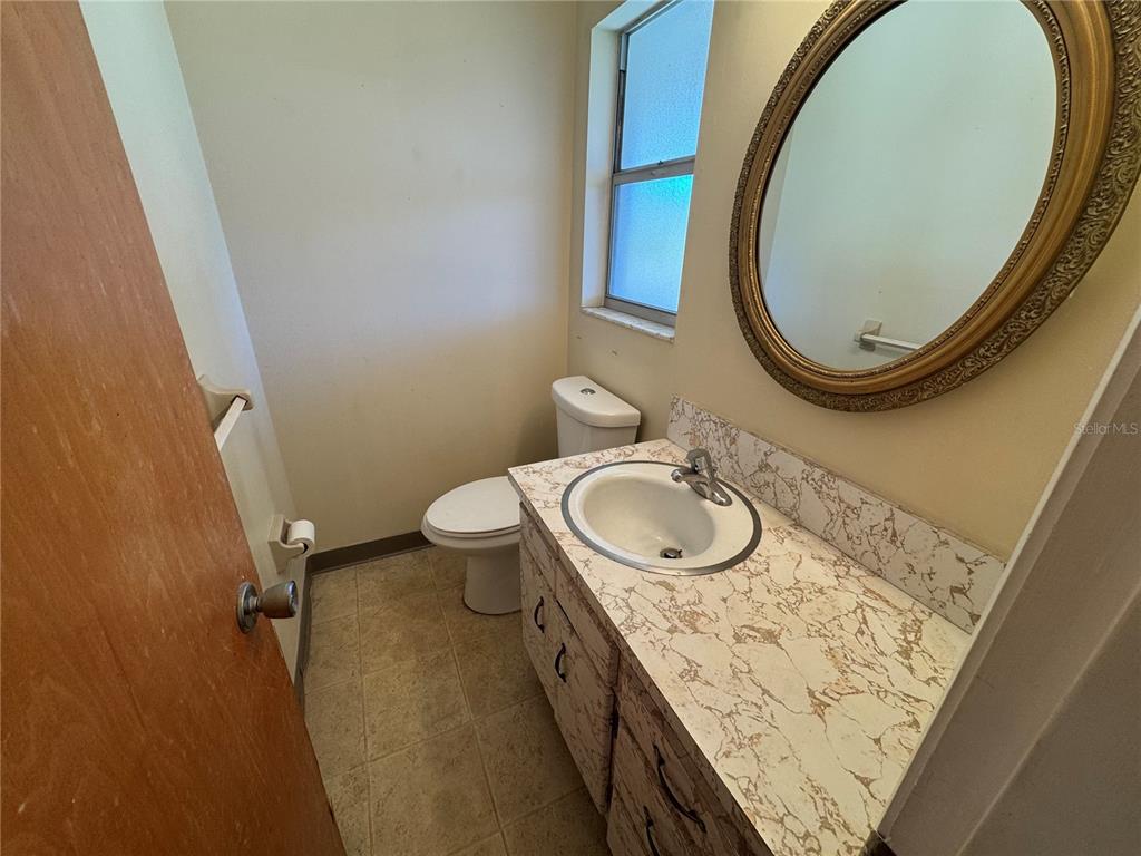 A bathroom features a vanity with a marble-look countertop, a round mirror, and a toilet — 245 CENTER ROAD UNIT 211, VENICE, FL