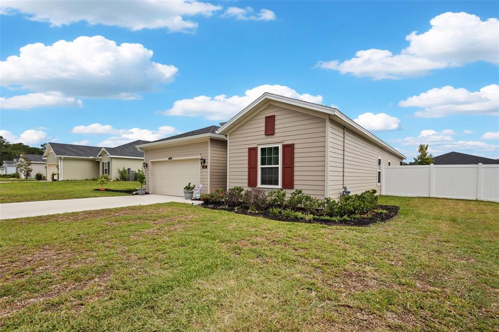 A tan single-story house with a two-car garage, red shutters, and a white vinyl fence — 560 NW 4TH AVENUE, WILLISTON, FL